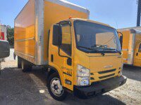 A bright yellow Isuzu box truck is parked outdoors on a sunny day, with sunlight reflecting off its windshield and the side of the truck. The truck is labeled with a U-Haul logo and various identification numbers.