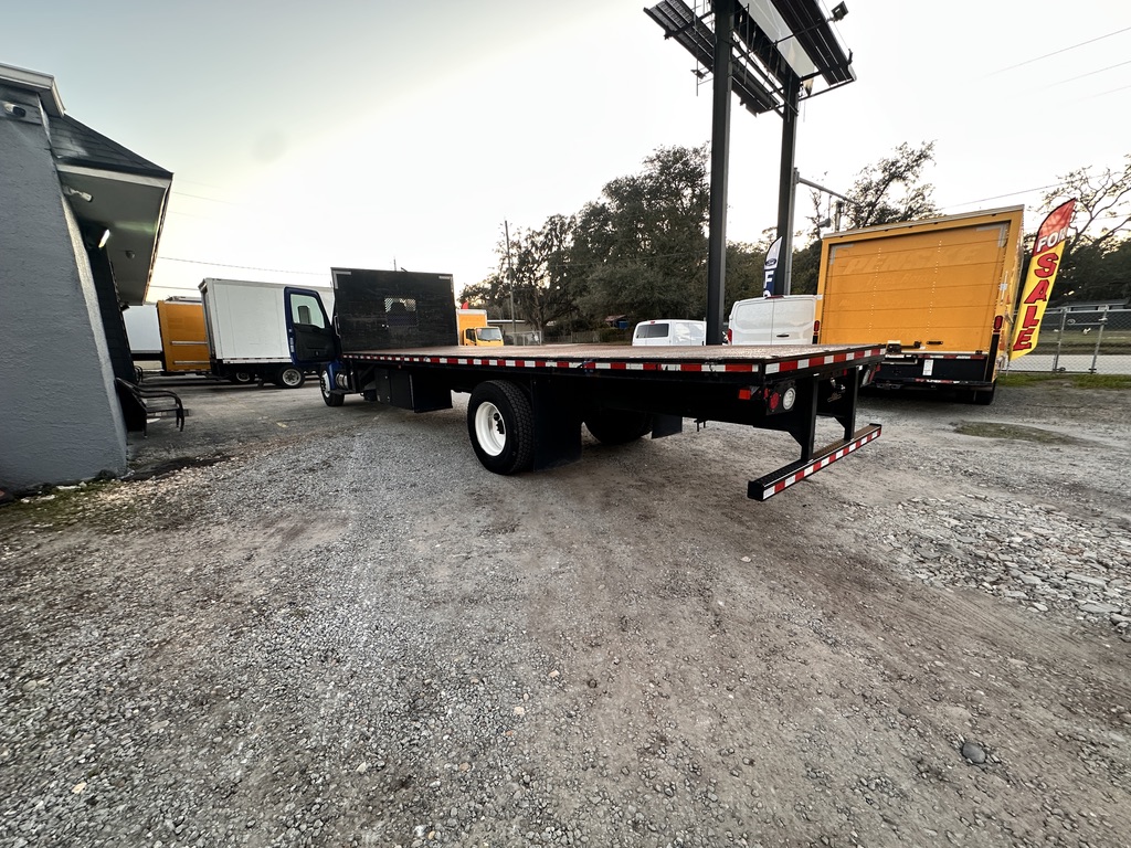 Flatbed truck with orange box truck and white truck in lot