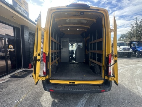 Rear view of an empty yellow Ford Transit cargo van with doors open.