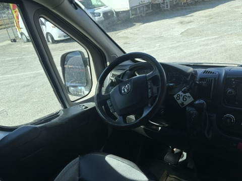 Interior view of a Ram ProMaster van dashboard, steering wheel, and side mirror.