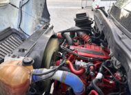Close-up of a Cummins diesel engine in a semi-truck, showing red engine block and hoses.