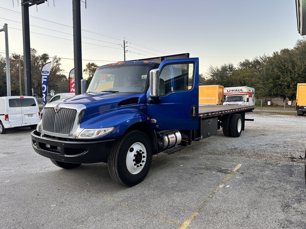 Blue flatbed truck with U-Haul trailer parked on asphalt lot