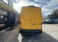 Yellow Ford Transit van parked outside a business with other vehicles.