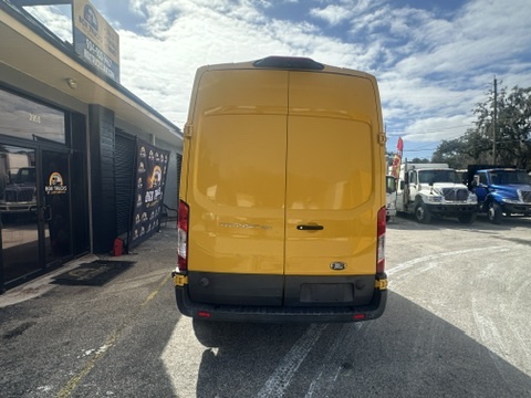 Yellow Ford Transit van parked outside a business with other vehicles.