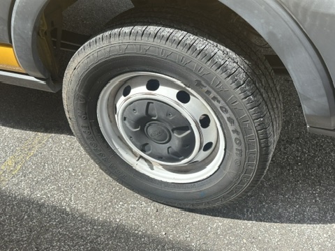 Close-up of a Firestone van tire on a gray rim, parked on asphalt.