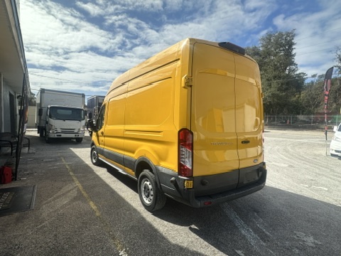 Yellow Ford Transit van parked outdoors on a sunny day.