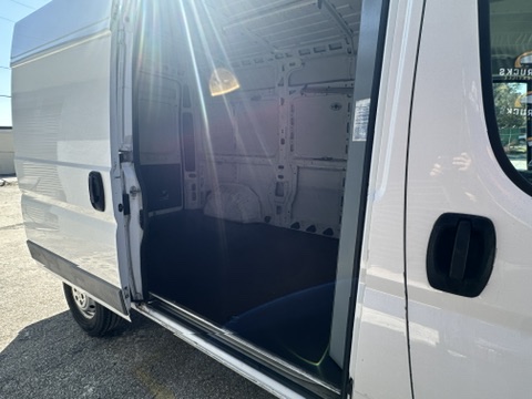 White cargo van interior with open sliding door, showing dark floor and shelving.
