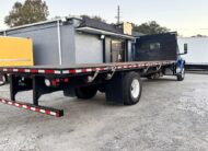 Blue flatbed truck with a large cargo bed parked on gravel