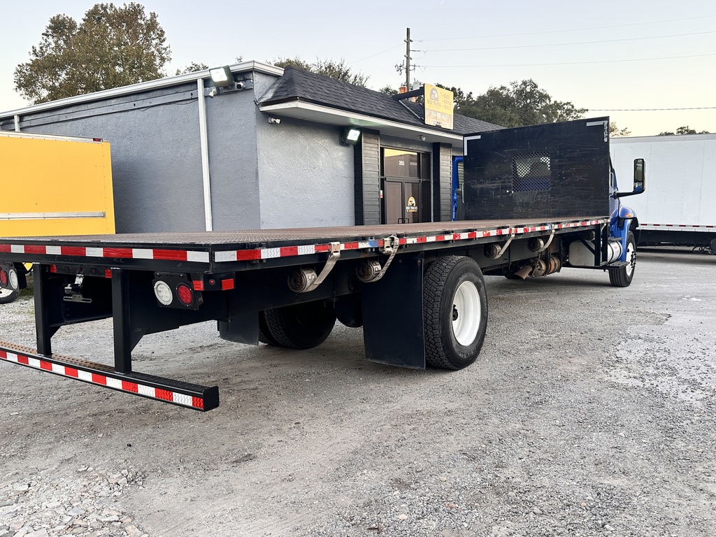 Blue flatbed truck with a large cargo bed parked on gravel