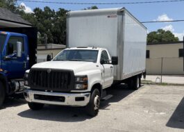 White box truck with black grille parked next to a blue truck