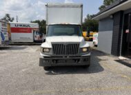 White U-Haul truck parked outdoors with other U-Haul vehicles and a building.