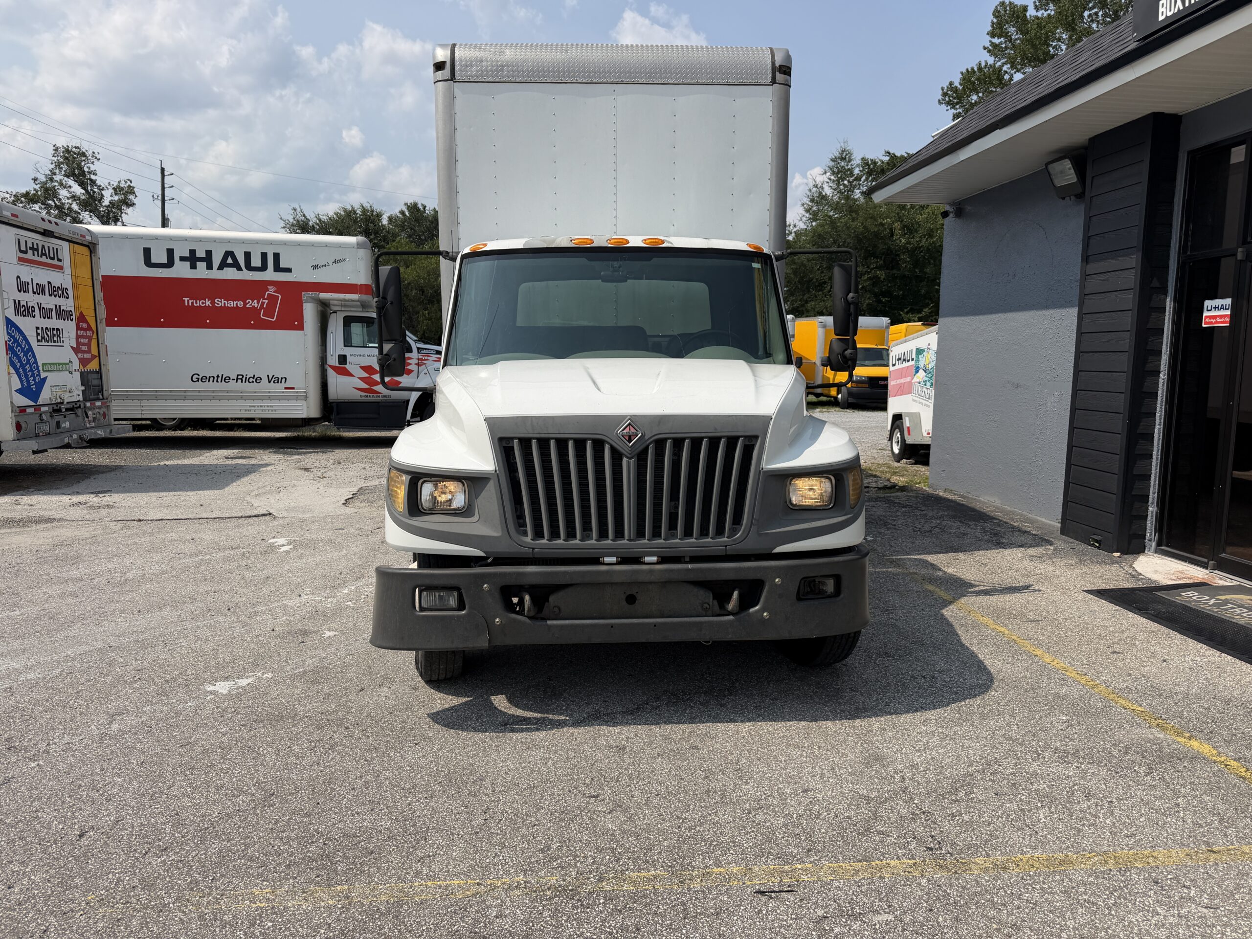 White U-Haul truck parked outdoors with other U-Haul vehicles and a building.
