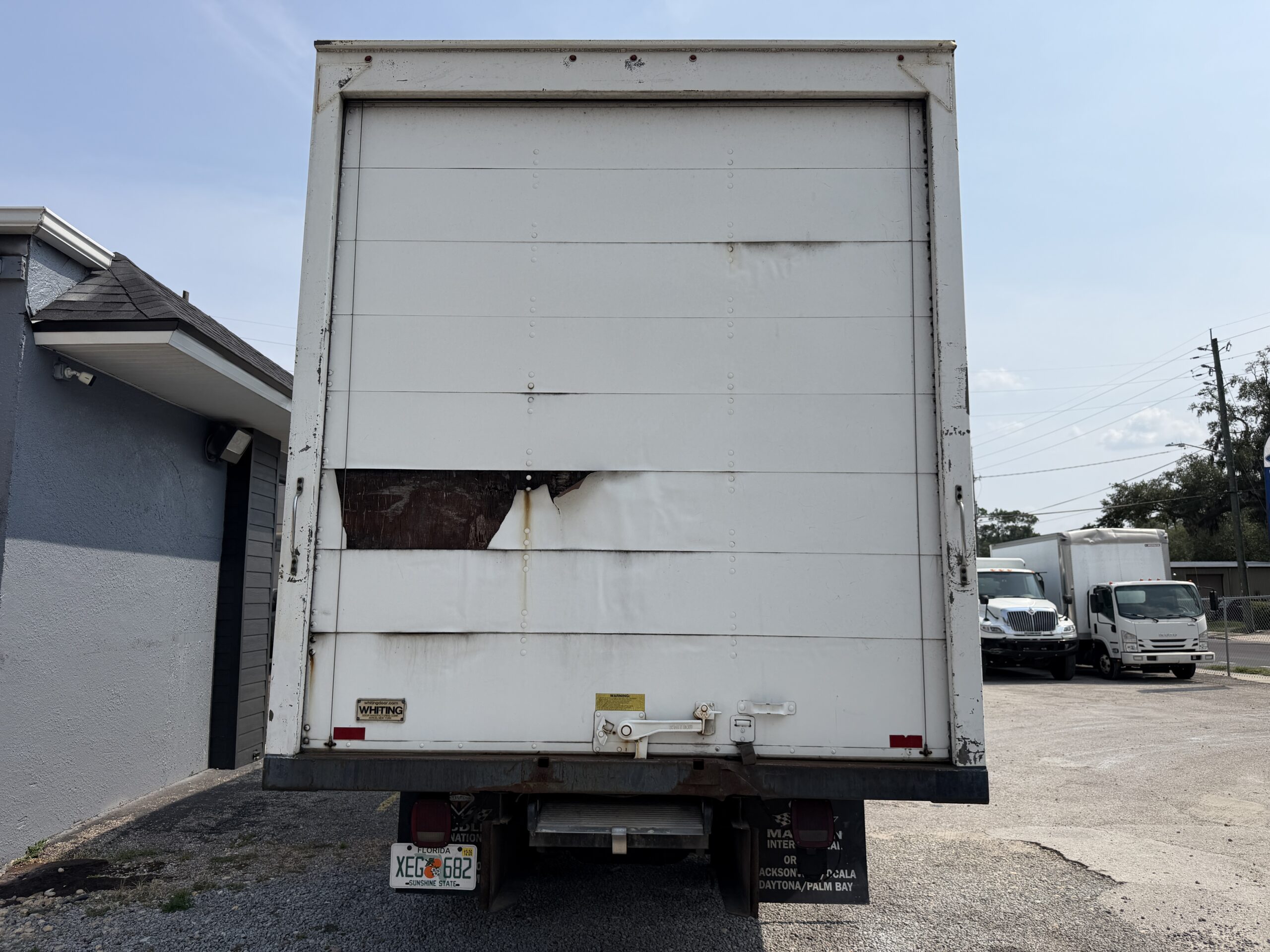 Rear view of a white box truck with a damaged panel, license plate XEG 682