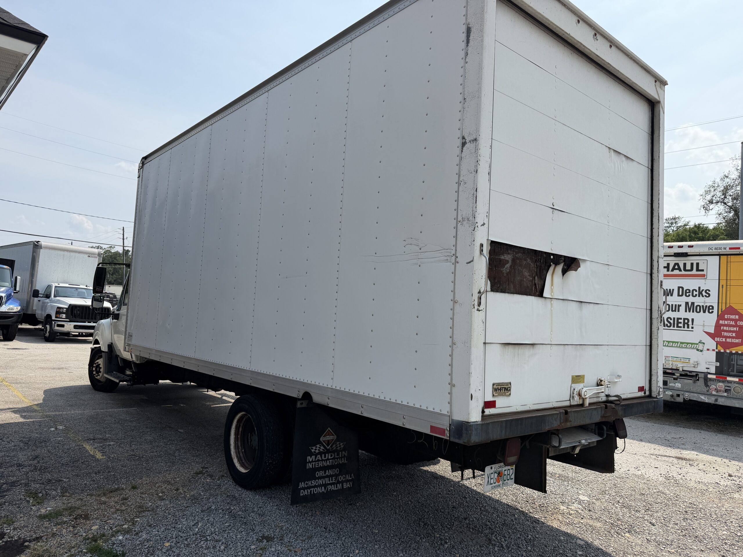 White box truck with damage on the rear door, parked outdoors.