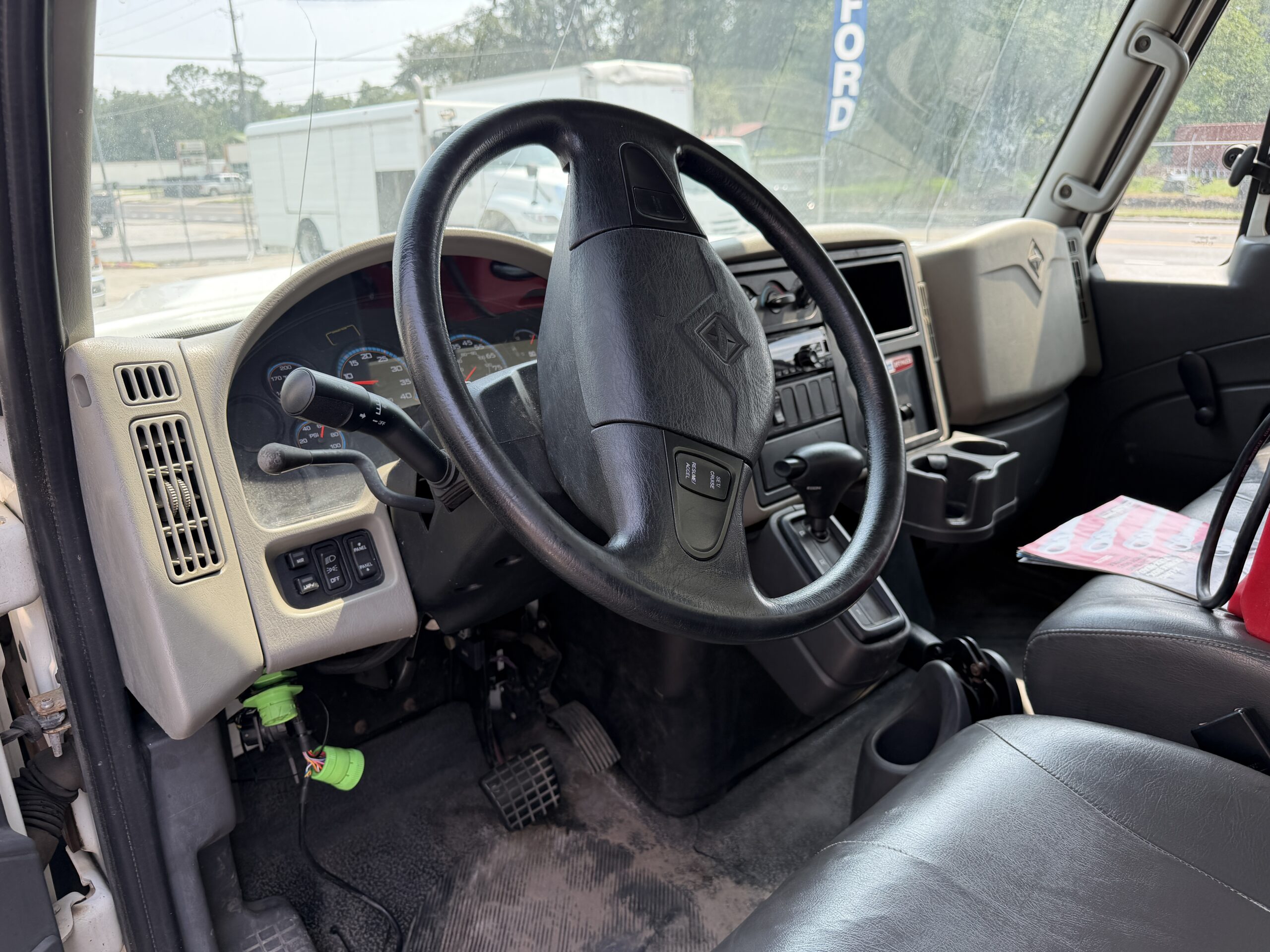 Interior of a commercial truck cab, showing the steering wheel, dashboard, and driver's seat.