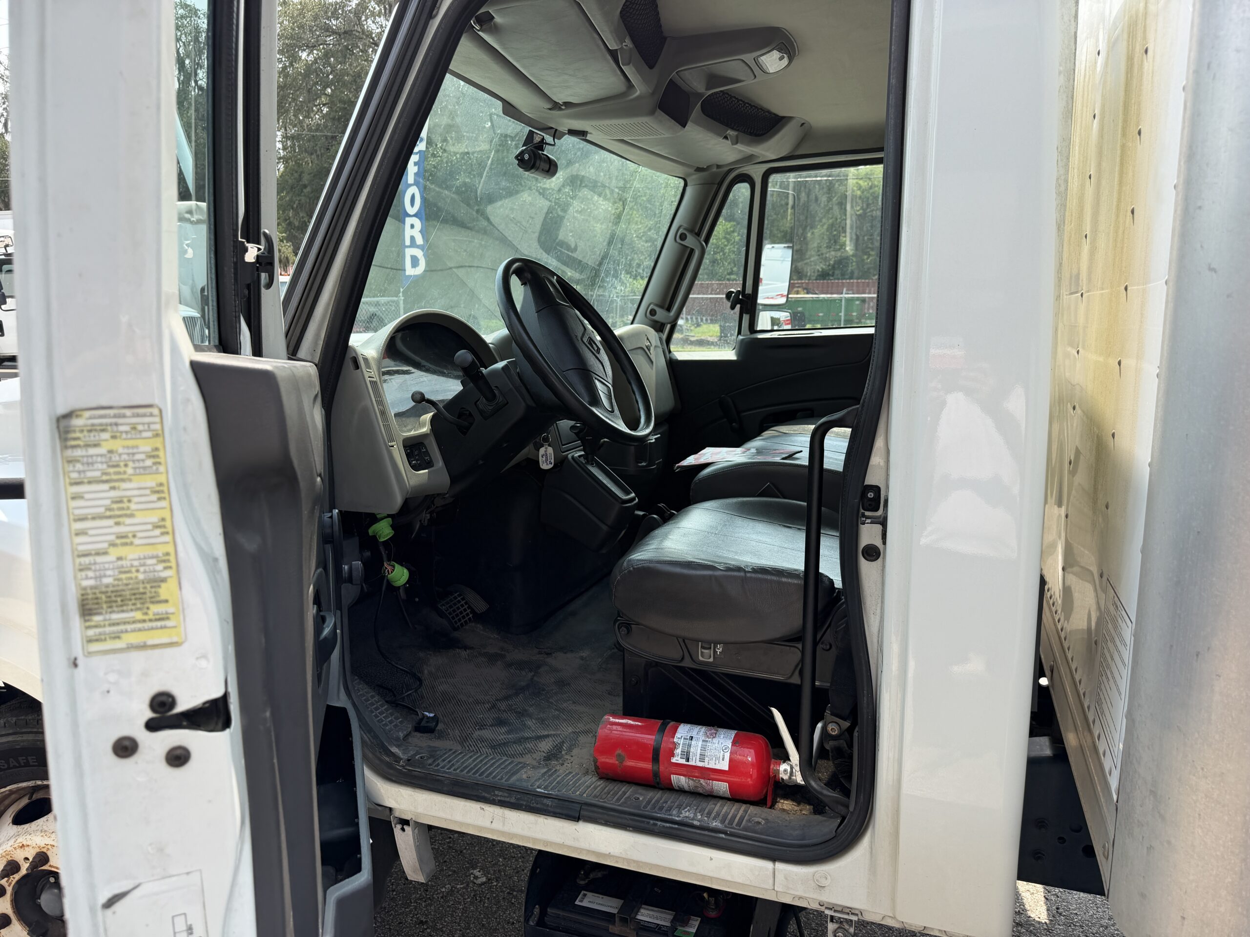 Interior view of a white box truck cab, showing seats, steering wheel, and fire extinguisher.