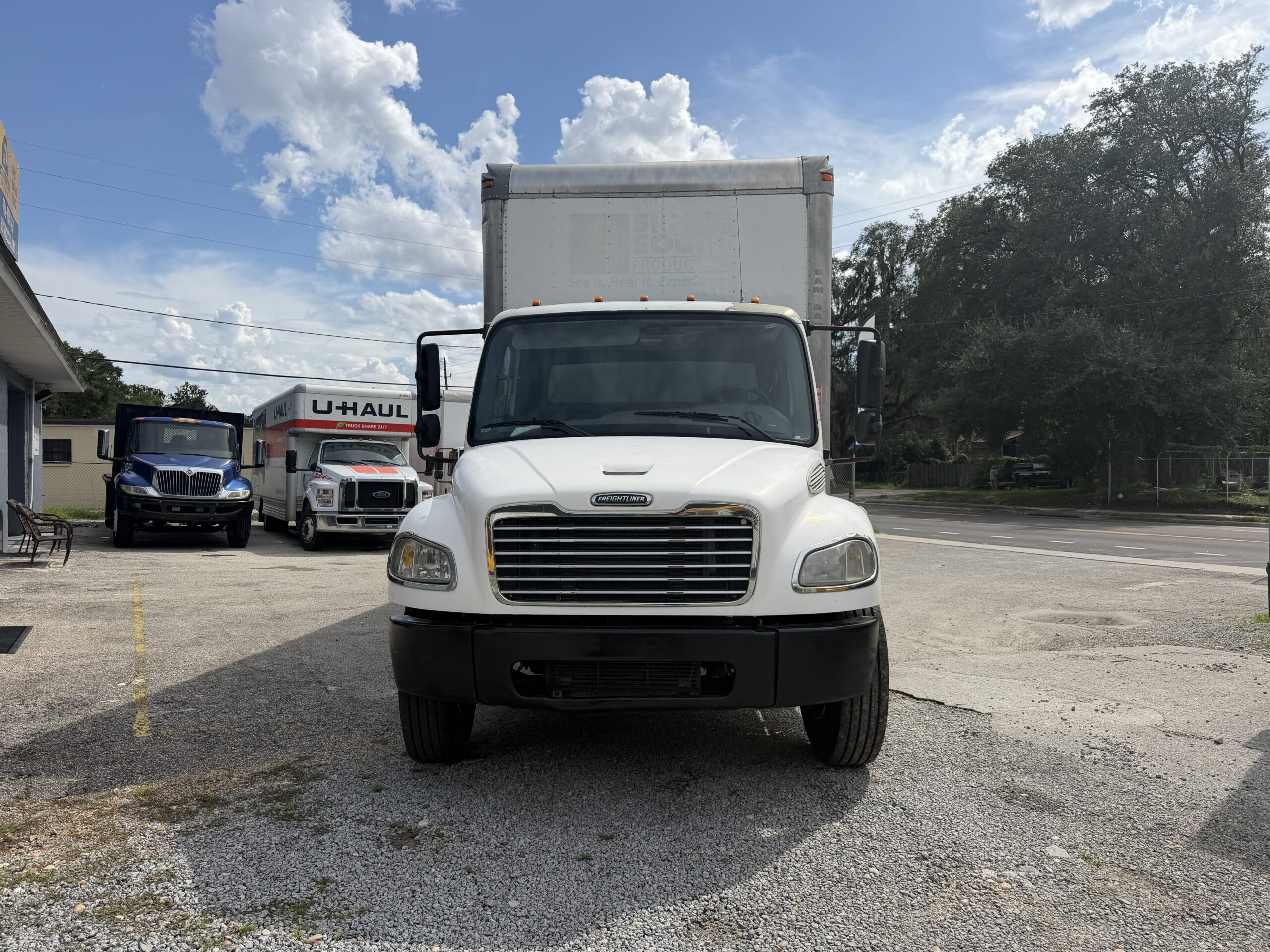 2007 Freightliner M2 26ft box truck front view, U-Haul trucks nearby.