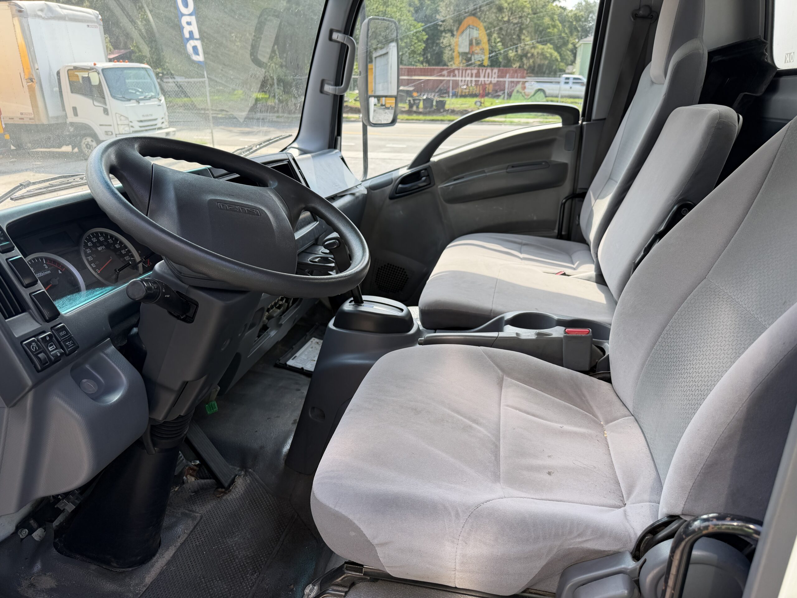 Interior view of a 2020 Isuzu NRR box truck, showing the driver's seat, steering wheel, and dashboard.
